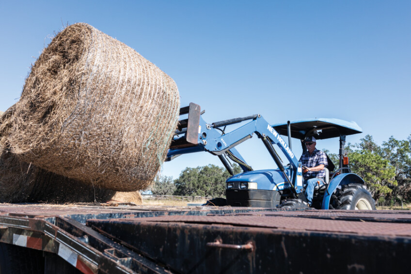 Chuck Johnston in a tractor loading round hay bales onto a trailer